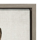 Close-up of a natural wood frame corner enclosing textured canvas with light neutral fabric and a small dark illustration detail in the corner.