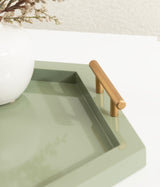 Hexagonal sage green tray with a smooth finish and a cylindrical brushed gold handle resting on a white surface.