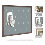 Square pinboard with muted blue fabric featuring a small repeating botanical leaf pattern and a dark wood frame, holding two black and white photos secured with wooden pins.