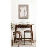 Wooden high table with two matching stools in a light room, featuring a framed abstract art print with cream organic shapes on a taupe background above the table.