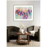 Abstract horizontal painting of multicolored vertical brushstrokes in pink, blue, orange, and teal above two dark gray armchairs and a round wooden coffee table with a vase of white flowers.