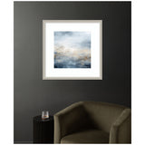 Framed abstract oceanic wall art featuring serene blue and beige tones with soft brushstrokes, hanging on a dark gray wall above an olive-green curved armchair and black side table.