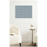 Light blue plaid fabric pinboard with white grid lines, framed in white, hanging centered on a plain white wall above a brass pedestal table and two off-white upholstered armchairs.