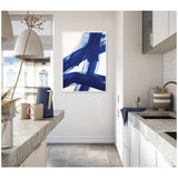 Framed abstract canvas featuring bold cobalt blue brushstrokes on white, hanging on a white kitchen wall between concrete countertops and light cabinetry.