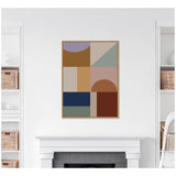 Framed abstract art print with geometric shapes in muted earth tones, including ochre, navy, mauve, and rust, hanging above a white fireplace in a minimalist living room.