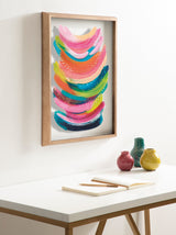 Colorful abstract art with curved brushstrokes in pink, green, blue, and yellow shades framed in light wood, hanging above a white desk with three small colorful vases.