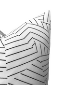 Corner view of a white pillow cover with an abstract black stripe pattern forming angular and segmented lines.