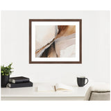 Framed abstract wall art with soft beige, brown, and gray tones hung above a white desk holding a black mug, open book, stacked books, and a green plant in a black pot.