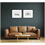 Two black-framed vintage postcard prints in black and white above a brown leather sofa, against a dark gray wall, with a wooden coffee table and dried floral centerpiece.