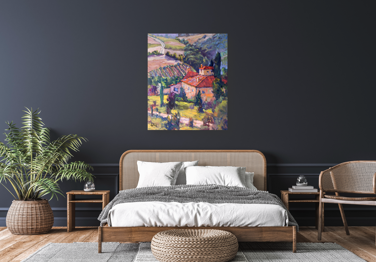 Colorful canvas print of a vineyard landscape with red-roofed buildings and green fields hanging on a dark blue wall above a bed with white and gray bedding in a modern bedroom setting with wicker furniture and a large potted fern
