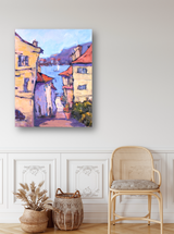 Impressionist canvas painting of narrow town street with beige buildings and red roofs leading to a blue water view under a soft purple sky.