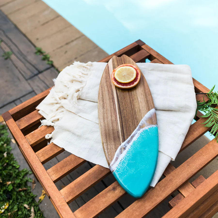 Wooden surfboard resin serving board with blue resin design on a wooden surface near a pool