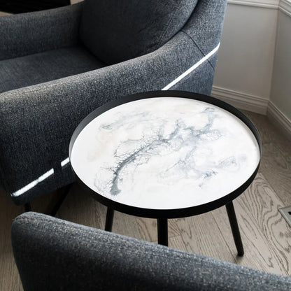 Gray armchair with a round marble resin table in a room with a fireplace and window.