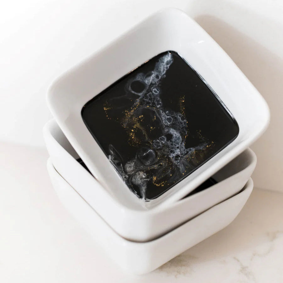 Two white resin square bowls stacked on a light surface with a dark interior.