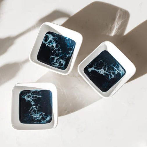 Three square resin ceramic tiles with blue abstract patterns on a marble surface