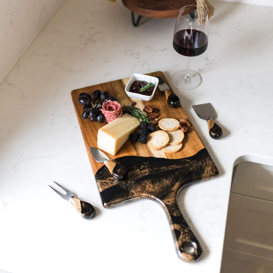 Wooden resin charcuterie board with cheese, grapes, and a glass of red wine on a white surface.