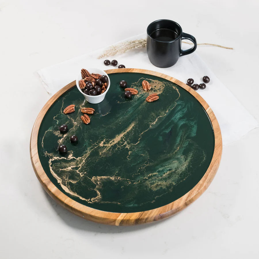 Round green resin lazy susan tray with wooden rim on a white surface, featuring a black mug and small bowl of nuts.