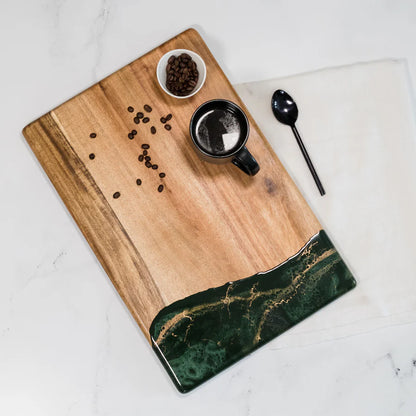 acacia resin serving bread board with green resin edge, coffee cup, spoon, and coffee beans on a white surface.