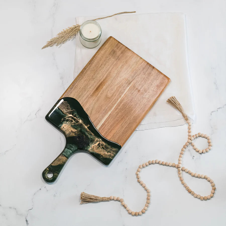 Wooden resin charcuterie board with green resin accents on a marble surface with a candle and decorative elements.