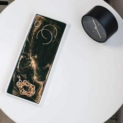 Marble-patterned resin ceramic tray with earrings on a white surface next to a black clock.