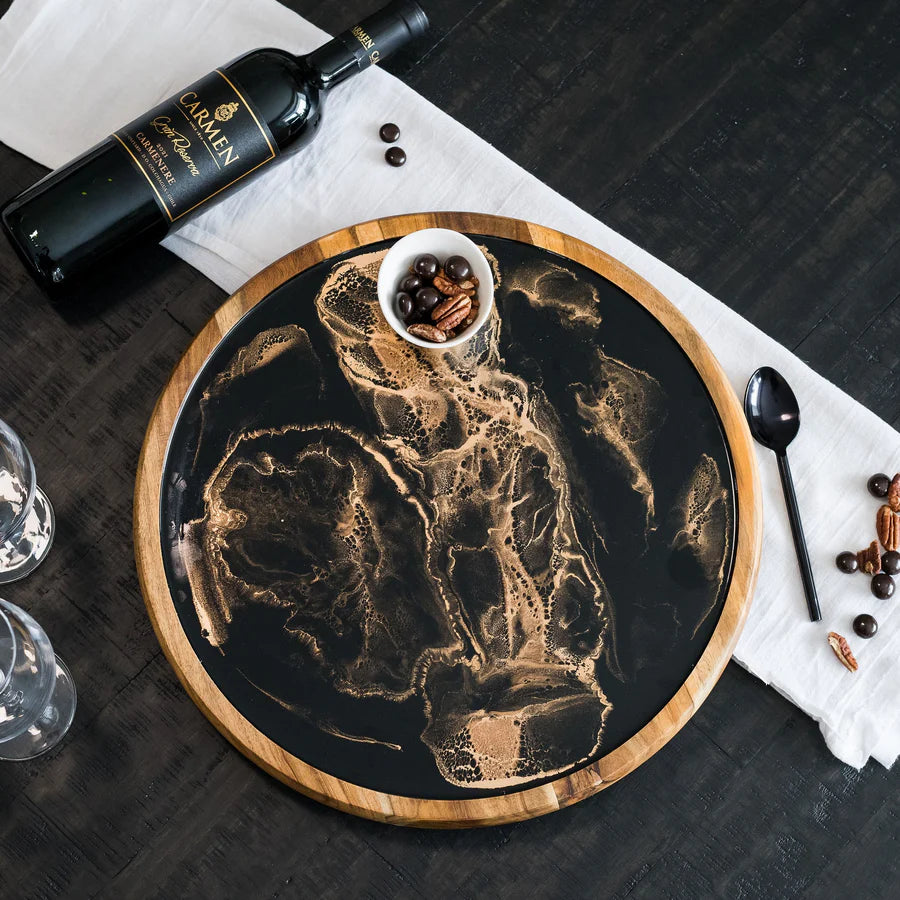 Decorative resin lazy susan tray with a black abstract design, accompanied by a bottle of wine and small bowl on a dark surface.