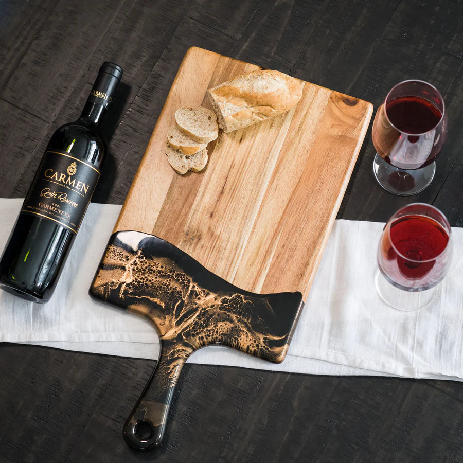 Wine bottle, resin charcuterie board with bread, and wine glasses on a dark surface