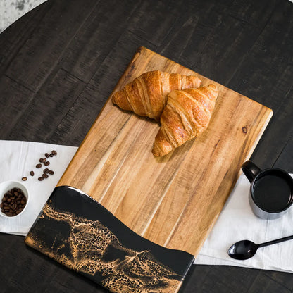 Wooden acacia resin serving bread board with croissants, coffee beans, and a cup of coffee on a dark surface.