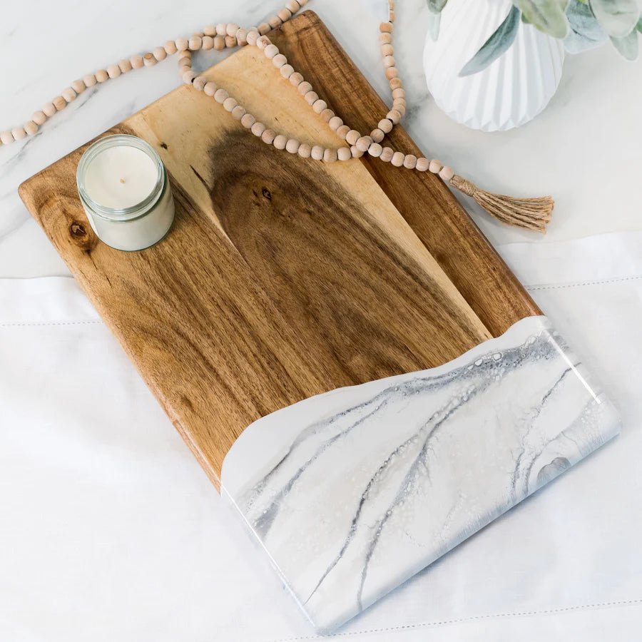 acacia resin serving bread board with a marble edge and a candle on a white surface