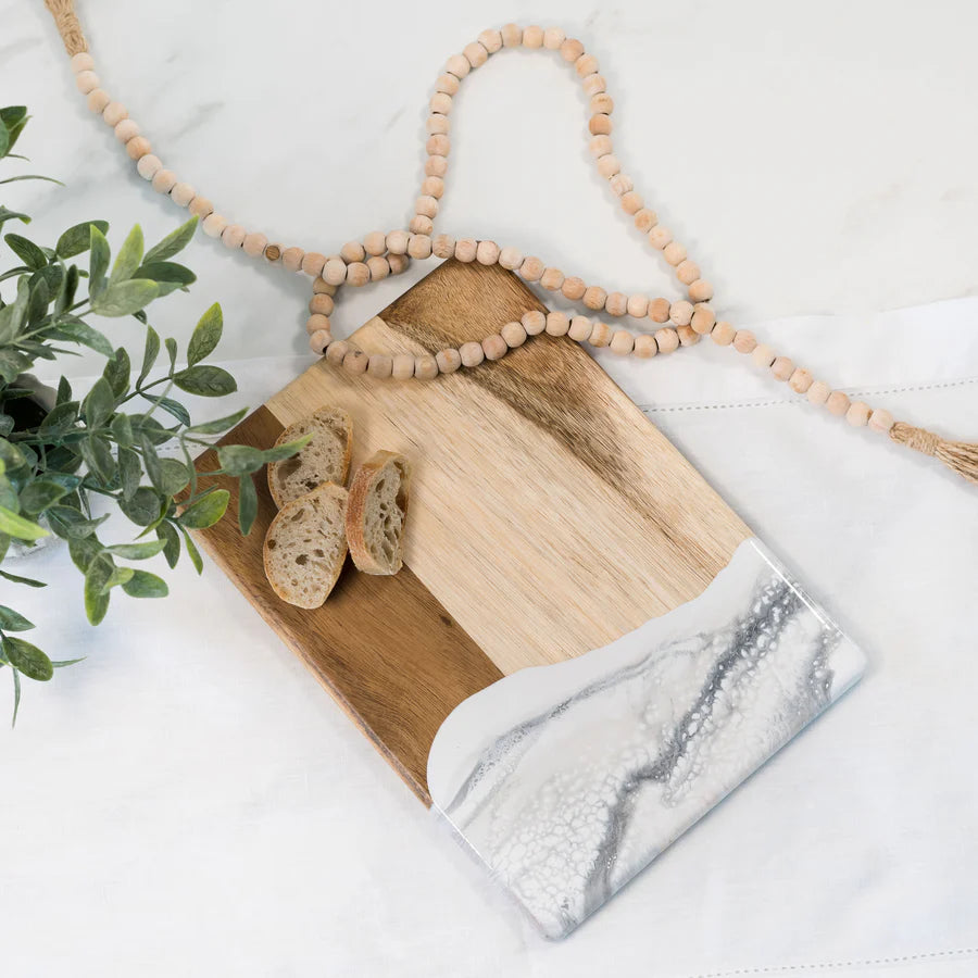 Wooden resin charcuterie board with marble accents and bread slices on a white surface with a plant.