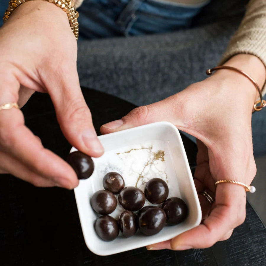 Person holding a small resin white dish with dark chocolates