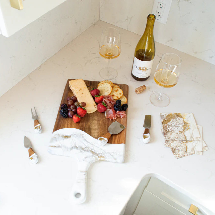 Wooden resin charcuterie board with cheese, fruits, and meats on a kitchen counter with wine and glasses.