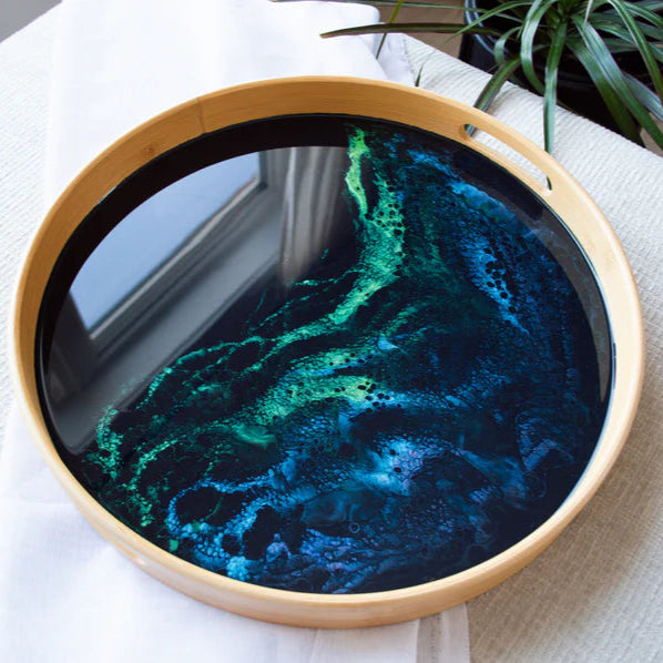 Round serving tray with blue and green resin design on a light surface.