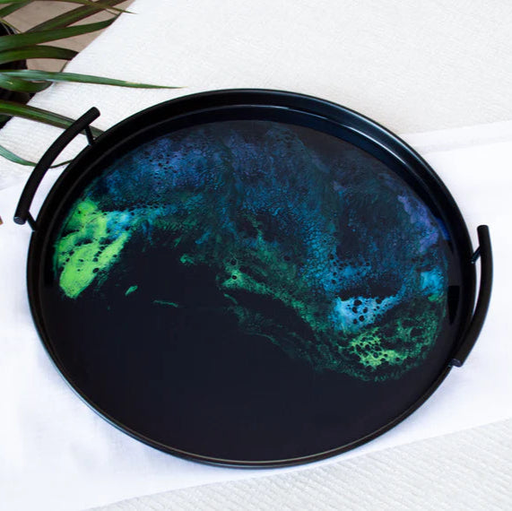 Round black resin tray with abstract green and blue design on a white surface