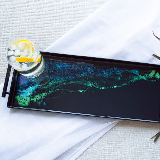 Decorative resin tray with a colorful abstract design on a white surface with a glass of lemonade.