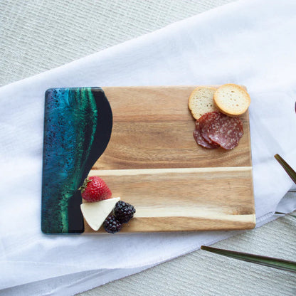 Wooden resin charcuterie board with a colorful resin design, placed on a white surface with a plant in the background.