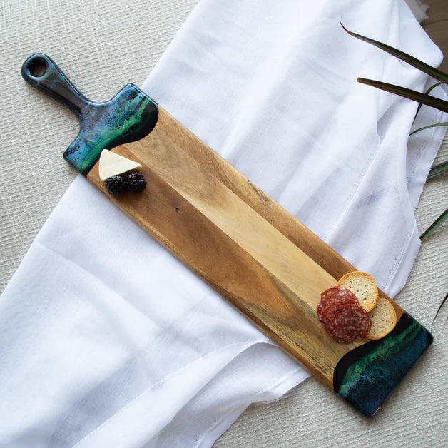 Wooden baguette resin serving tray with decorative handles on a white cloth with a plant in the background