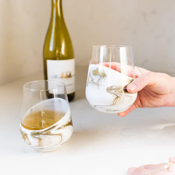 Person holding a resin wine glass with white wine next to a bottle on a light surface.