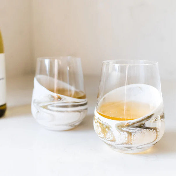 Wine bottle and two resin wine glasses with white wine on a light surface