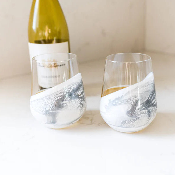 Two resin wine glasses with marble design on a white surface next to a bottle of wine.