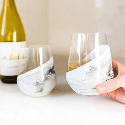 Hand holding a resin wine glass with a bottle of white wine in the background