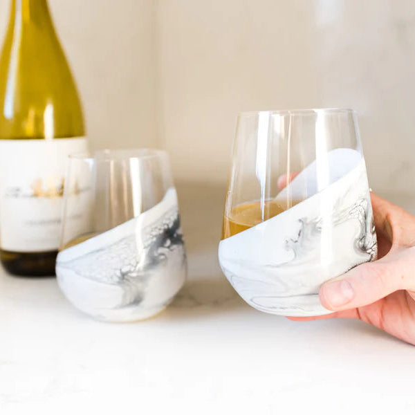 Hand holding a resin wine glass with a bottle of white wine in the background