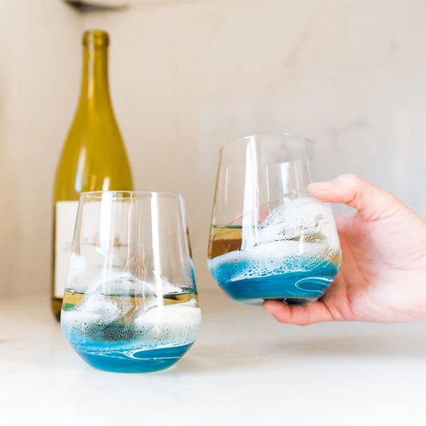 Two resin wine glasses with blue and white liquid on a table with a bottle in the background
