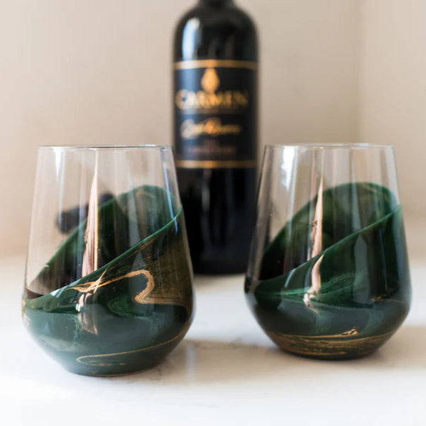 Two green stemless resin wine glasses with a bottle of Chardonnay in the background.