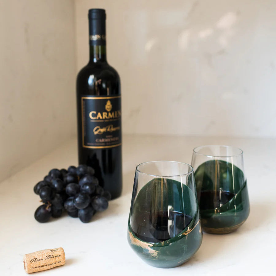 Bottle of Carmelo wine with two resin wine glasses and grapes on a white surface