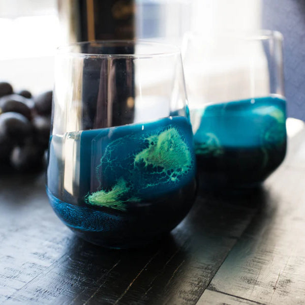 Two glasses with blue and green resin design sitting on a wooden surface
