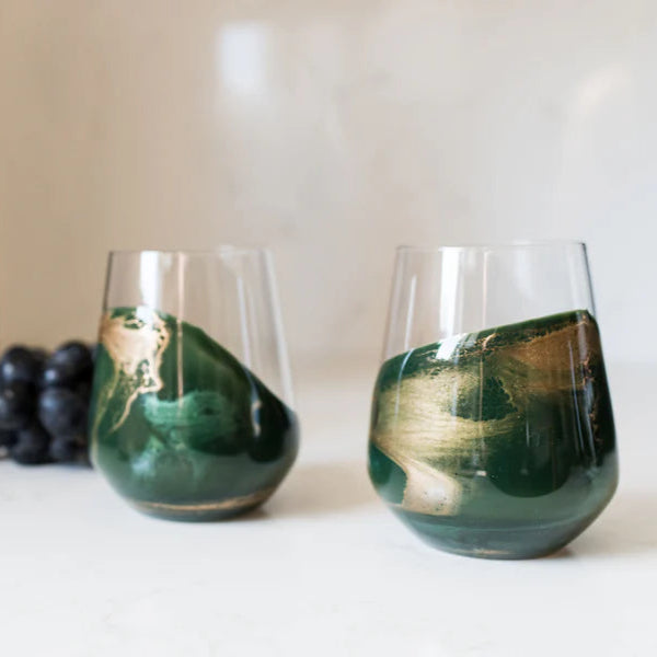 Two green stemless resin wine glasses with a bottle of Calvados and grapes on a white surface.
