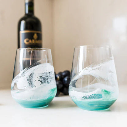 Two stemless resin wine glasses with blue and white design on a table with a bottle and grapes in the background.