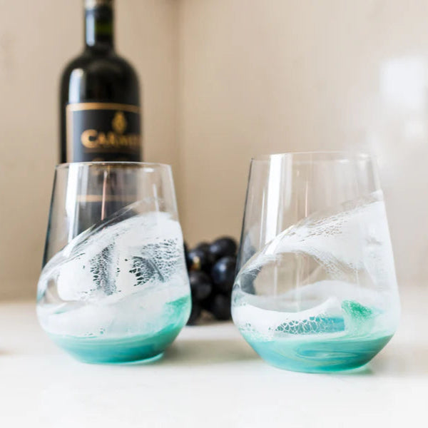 Two stemless resin wine glasses with blue and white design on a table with a bottle and grapes in the background.
