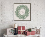 Green wreath with pine leaves and small pine cones surrounding the word 'JOY' in a simple black frame on a white brick wall above a mantel with wrapped gifts and a candle.