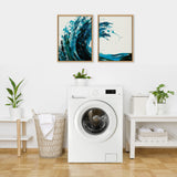 Two framed abstract blue wave paintings with swirling brushstrokes hang side by side above a white washing machine in a bright laundry room